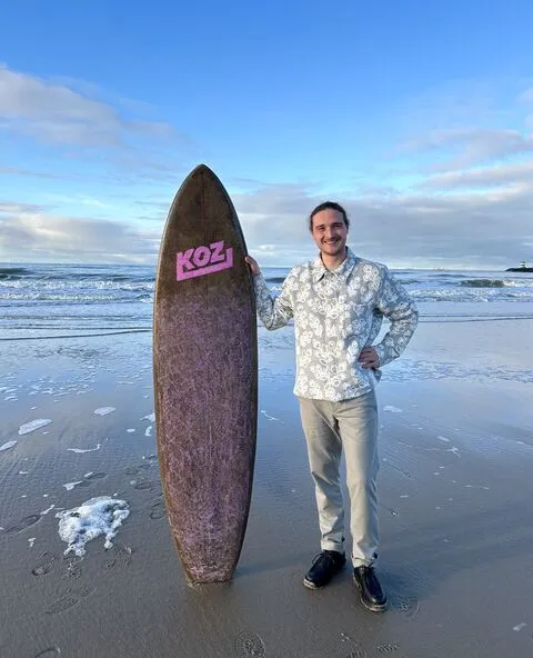 Andy Cartier with a mycelium surfboard on the beach, ocean in the background