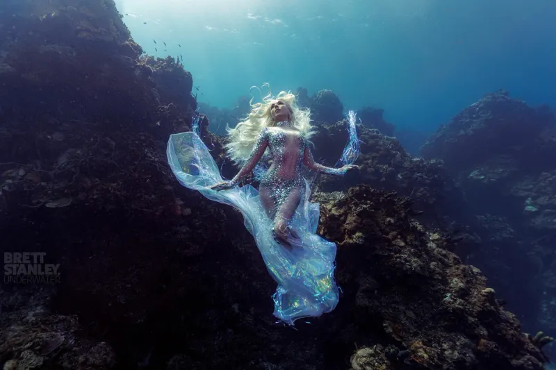 Hannah Mermaid floating between dark underwater rock formations