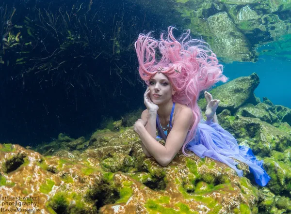 Hannah Mermaid on a sunlit reef in pink hair and a purple tail