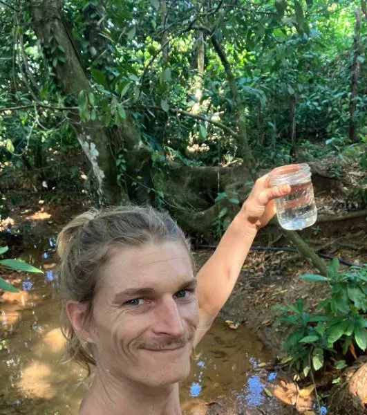 Arthur Ara holding a jar of clean water beside a creek in the Baru watershed