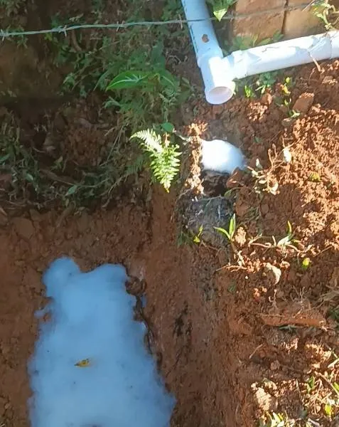 Soapy greywater runoff pooling below a household drain pipe before filter installation