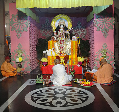 photograph of devotees praying at lifesize sculpture of Saraswati playing a sitar